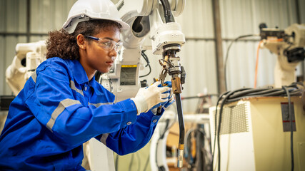 African american engineer woman fixing and testing an Artificial Intelligent welding robotic automatic arm machine in modern technology factory. Automation manufacturing for industry 4.0 Technology.