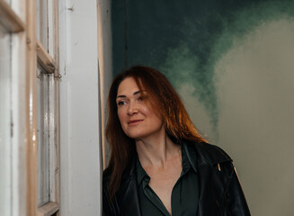 Fototapeta premium Caucasian mature female in leather jacket by window looking thoughtful