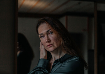 Thoughtful mature caucasian woman in green shirt in dimly lit room