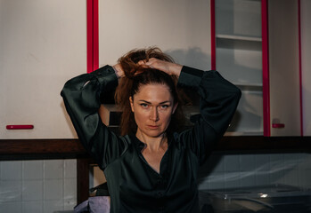 Caucasian female adult adjusting hair in dimly lit kitchen with cabinets