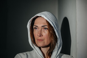 Contemplative caucasian female in white hooded attire leaning against wall