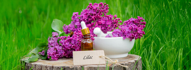 Lilac essential oil on a wooden stump. Bottle with aromatic oil and lilac flowers