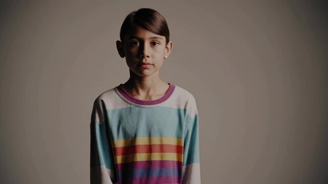 Young girl standing expressionless in colorful striped sweater  