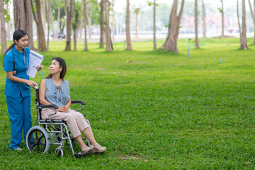 Fototapeta premium Woman doctor is taking an elderly person in wheel chair to relax in park help elderly person relax after elderly person injured his ankle and could not walk by himself.doctor takes patient wheel chair