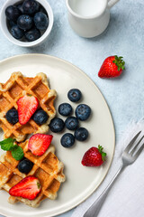 Belgian waffles with strawberries and blueberries on a white plate. Top view, close-up. Clean composition in neutral tones.