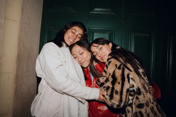 A multinational group of young women hugging warmly at a girls' party, standing outdoors against a...