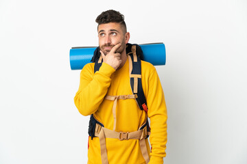 Young mountaineer man with a big backpack over isolated background having doubts