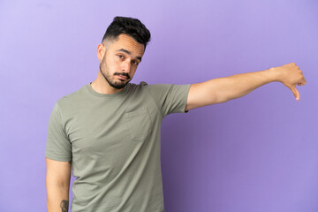 Young caucasian man isolated on purple background showing thumb down with negative expression