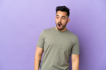 Obraz premium Young caucasian man isolated on purple background doing surprise gesture while looking to the side