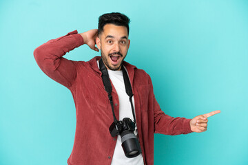 Young photographer caucasian man isolated on blue background surprised and pointing finger to the side