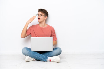 Teenager Russian man holding pc sitting on the floor isolated on white background yawning and...