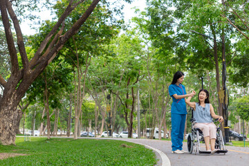 female doctor is taking an elderly person in wheelchair to relax in park help elderly person relax after elderly person injured his ankle and could not walk by himself. doctor takes patient wheelchair
