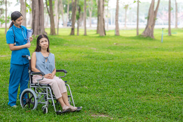 female doctor is taking an elderly person in wheelchair to relax in park help elderly person relax after elderly person injured his ankle and could not walk by himself. doctor takes patient wheelchair
