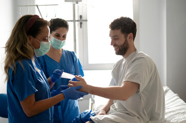 Nurses bandaging patient's hand in hospital room