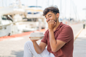 Young Arabian handsome man at outdoors taking a box of takeaway food