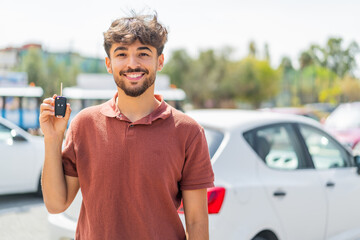 Young Arabian handsome man holding car key at outdoors smiling a lot © luismolinero