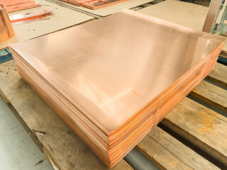 Stack of shiny copper sheets lying on wooden pallet in metalworking plant