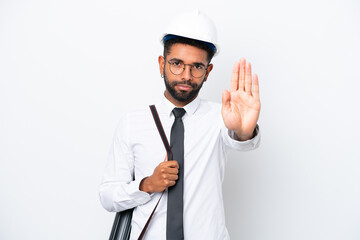 Young architect Brazilian man with helmet and holding blueprints isolated on white background making stop gesture