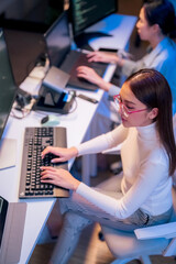 Plakat asian female programmer sits a dark tech workspace at night, fully focused on developing an online project. She writes HTML scripts and code for a modern website while contributing to automation work