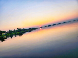 Sunset reflecting on the water with trees and a house on the shore