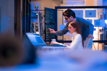 Asian programmers collaborating on software development at night, focused on writing code across...