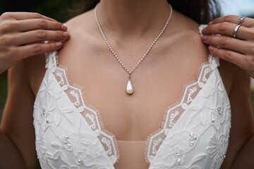 Bridal elegance: a close-up of a woman showcasing a delicate pearl necklace against her lace gown.