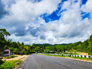 Road stretches through a lush green landscape under a cloudy sky
