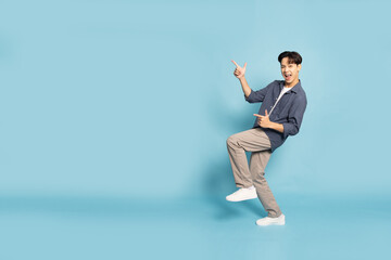 Happy Young Asian man smiling and pointing to empty copy space isolated on sky blue background,...