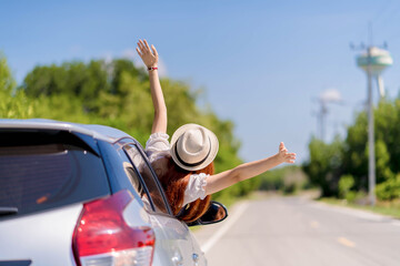 Happy young woman enjoying a summer road trip with arms out of car window, feeling free and joyful while traveling on a bright sunny day through the countryside.