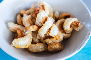Close-up of crispy pork rinds in a white bowl, a savory and crunchy snack made from fried pork skin, popular in various cuisines around the world.