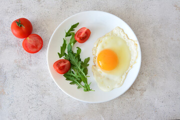 Fried egg with yellow yolk and tomatoes and arugula on a white plate