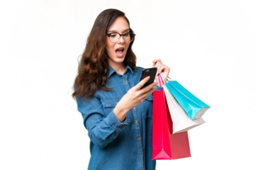 Young caucasian woman over isolated background holding shopping bags and writing a message with her cell phone to a friend