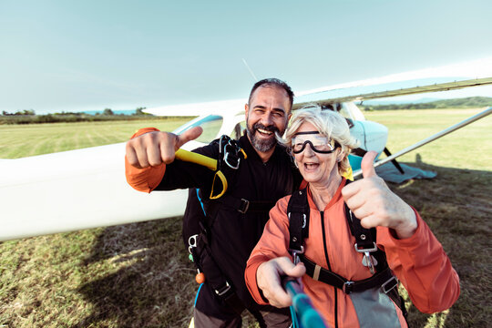 Senior woman taking a selfie with her male skydiving instructor before skydiving in an airplane on a open field