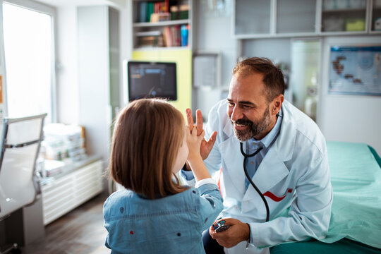 Happy pediatrician giving high five to child patient during doctor visit in medical clinic