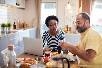 Couple discussing finances over breakfast with laptop at home kitchen table