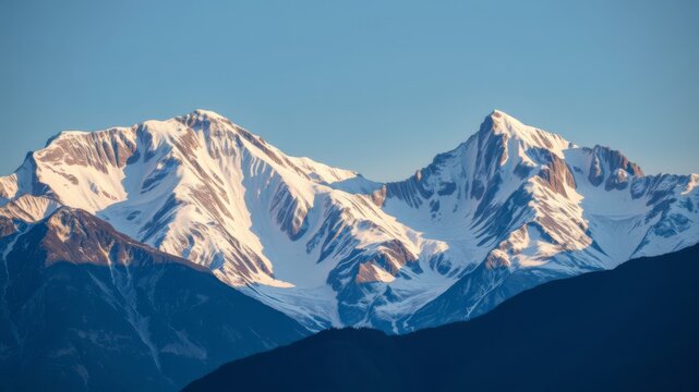 Majestic snow-capped mountain peaks rise dramatically against a clear vibrant blue sky at sunrise creating a breathtaking landscape.
