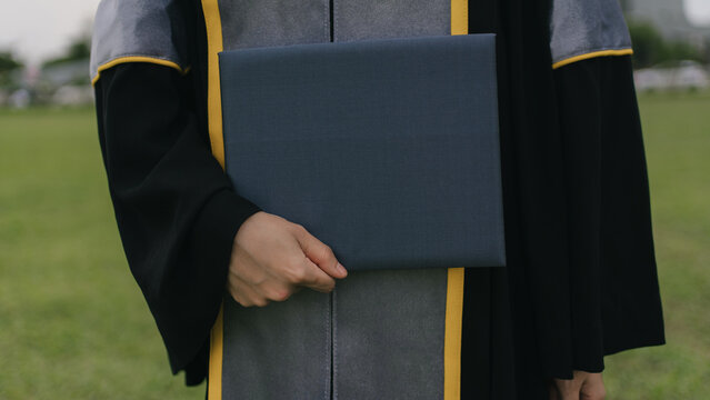 Close-up of a graduate holding a diploma folder in gown, symbolizing academic achievement, success, and new beginnings on a graduation day. - Powered by Adobe