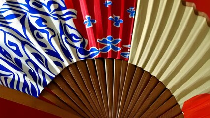 Close-up of traditional oriental hand fans featuring red, white, and blue floral patterns with wood frames and neutral colored paper panels. - Powered by Adobe
