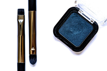 Flat lay of two parallel eyeshadow brushes and a gray-blue eyeshadow palette on white background....
