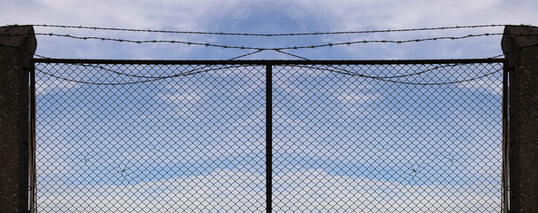 net fence with barbed wires against cloudy blue sky background. Chain link fence with sharp barb...