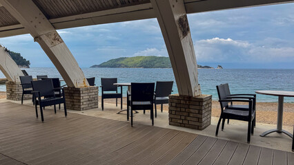  Scenic beachfront view from a modern terrace with empty chairs and tables overlooking the calm ocean waves