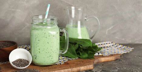 Mason jar of fresh spinach smoothie and bowl with chia seeds on grey background