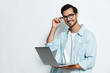 Smiling man wearing glasses holding laptop with hand on chin, expressing confidence and readiness,...