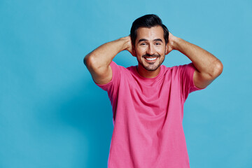Full body smiling happy cheerful young man wearing pink t-shirt joyfully posing with hands behind...