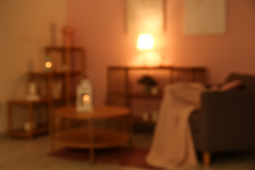 Blurred view of dark living room with table, armchair and glowing lamps near beige wall