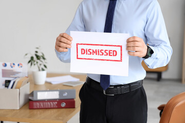 Young man holding paper with word DISMISSED in office