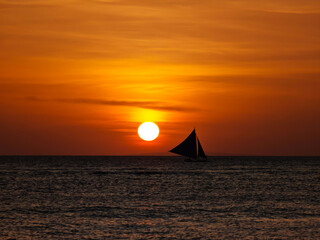 Boracay island sunset view with sailboat in horizon. Amazing topical sunset during a golden hour in...