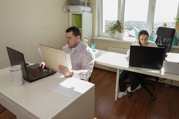 Coworking at home with natural sunlight streaming through the window as two people collaborate and complete parallel tasks at their respective desks