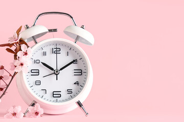 Alarm clock and blooming branch on pink background. Spring time