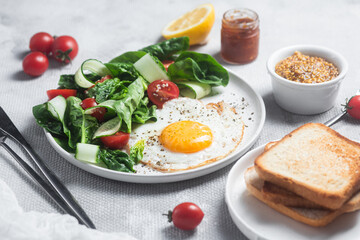 Fried egg with spinach, tomato and cucumber salad in a white plate. Healthy breakfast